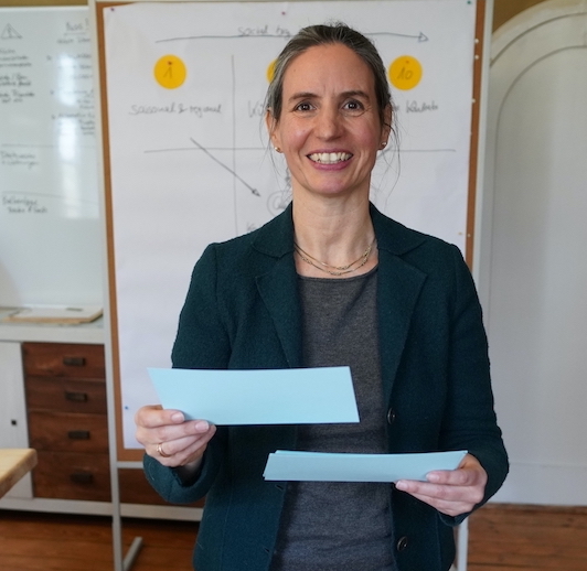 Pamela Wieckmann vor Whiteboard mit Papierkarten in der Hand